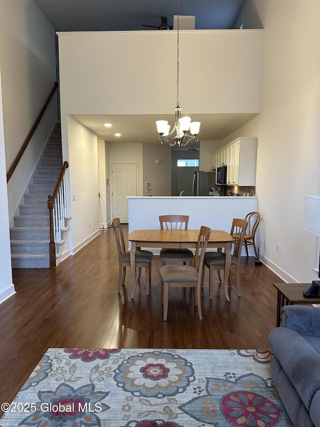 dining area featuring baseboards, dark wood finished floors, a towering ceiling, a notable chandelier, and stairs