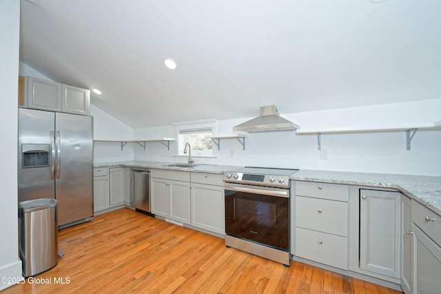 kitchen with a sink, lofted ceiling, light wood-style flooring, wall chimney exhaust hood, and appliances with stainless steel finishes