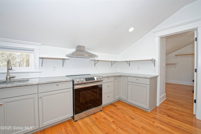 kitchen with stainless steel range with electric cooktop, lofted ceiling, wall chimney range hood, a sink, and light wood-style flooring