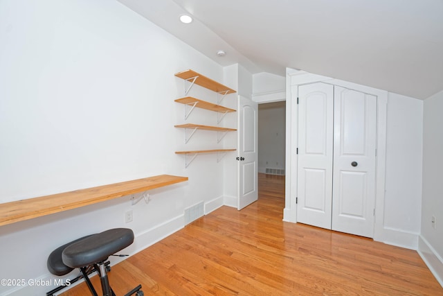 unfurnished office with light wood finished floors, baseboards, visible vents, and lofted ceiling