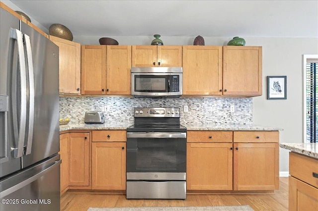 kitchen featuring backsplash, light stone countertops, appliances with stainless steel finishes, and light wood-style flooring