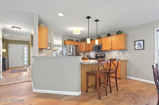 kitchen featuring a kitchen bar, appliances with stainless steel finishes, tasteful backsplash, light wood-type flooring, and a peninsula