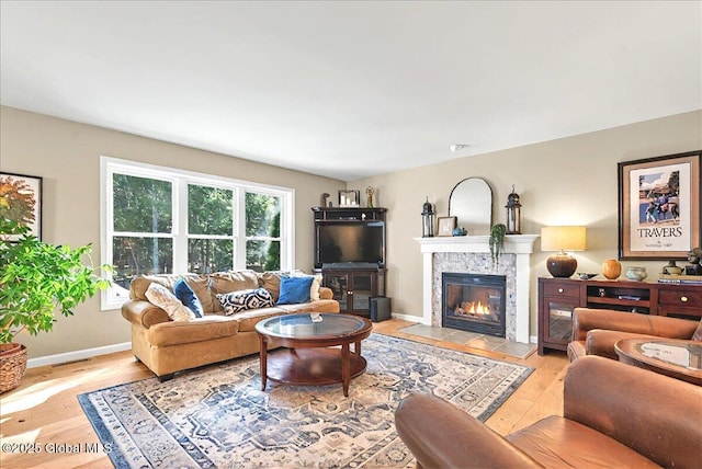 living area with a tiled fireplace, baseboards, wood finished floors, and visible vents