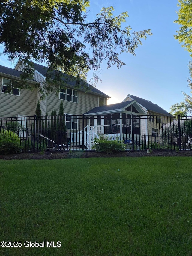rear view of house with a lawn, fence, and a sunroom