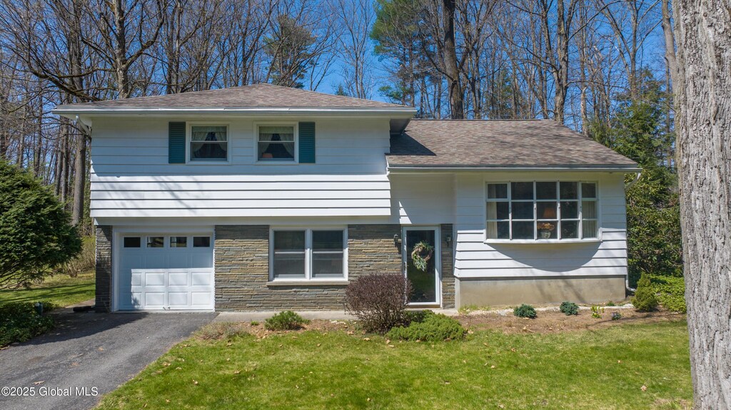 split level home with a garage, aphalt driveway, a front yard, and roof with shingles