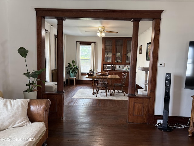 interior space featuring ceiling fan, dark wood-style flooring, and decorative columns