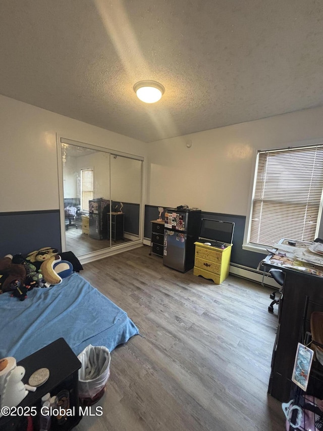 bedroom with a closet, a baseboard radiator, a textured ceiling, and wood finished floors