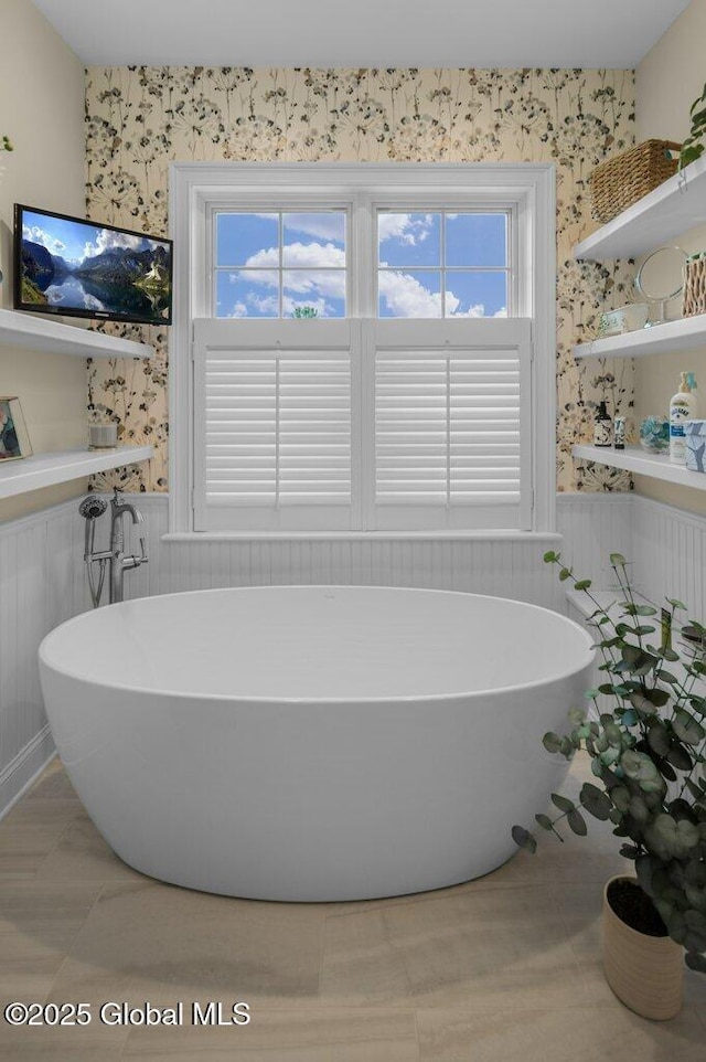 full bath with a soaking tub, wallpapered walls, wainscoting, and a healthy amount of sunlight