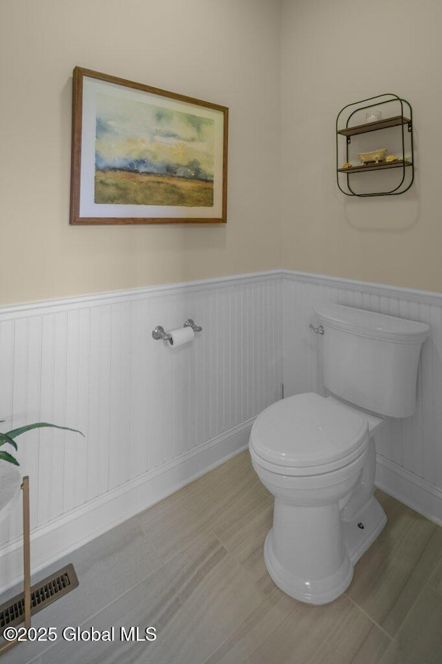 half bathroom featuring toilet, visible vents, and a wainscoted wall