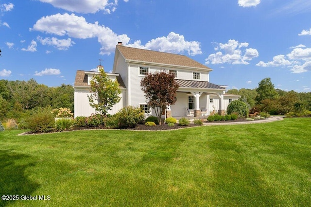 view of front of home featuring a front yard, a chimney, a standing seam roof, covered porch, and metal roof