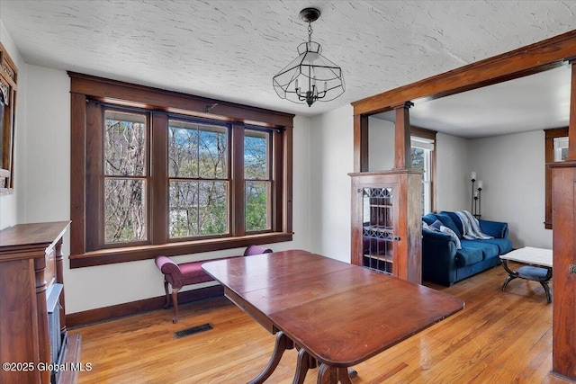 dining area featuring visible vents, light wood-style flooring, baseboards, and a chandelier
