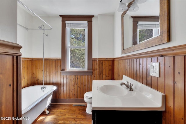 bathroom featuring wooden walls, a wainscoted wall, a freestanding tub, wood finished floors, and visible vents
