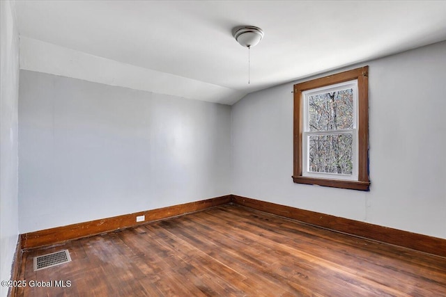 empty room featuring visible vents, baseboards, lofted ceiling, and hardwood / wood-style flooring