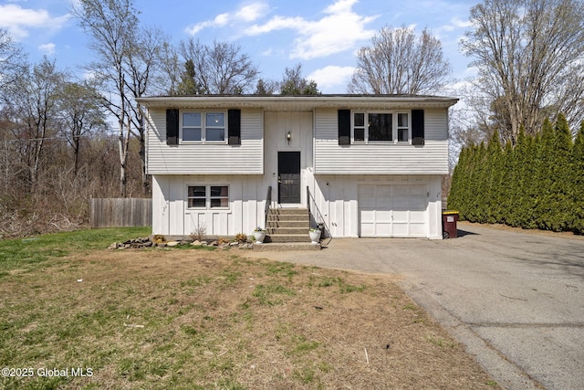 bi-level home with a front lawn, driveway, fence, entry steps, and a garage