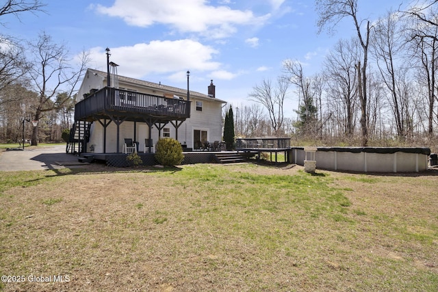 rear view of house featuring a chimney, a covered pool, a deck, and a lawn