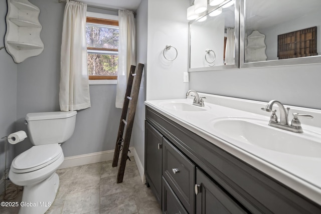 full bathroom featuring baseboards, a sink, double vanity, and toilet