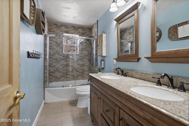 bathroom featuring toilet, a sink, double vanity, and combined bath / shower with glass door