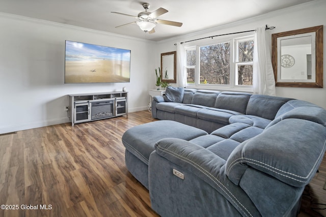 living area featuring wood finished floors, baseboards, ceiling fan, and crown molding