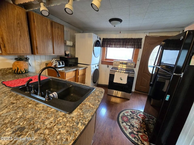 kitchen featuring a sink, stacked washing maching and dryer, black appliances, dark wood finished floors, and brown cabinetry