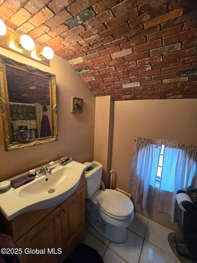 bathroom with vanity, tile patterned floors, toilet, lofted ceiling, and brick ceiling