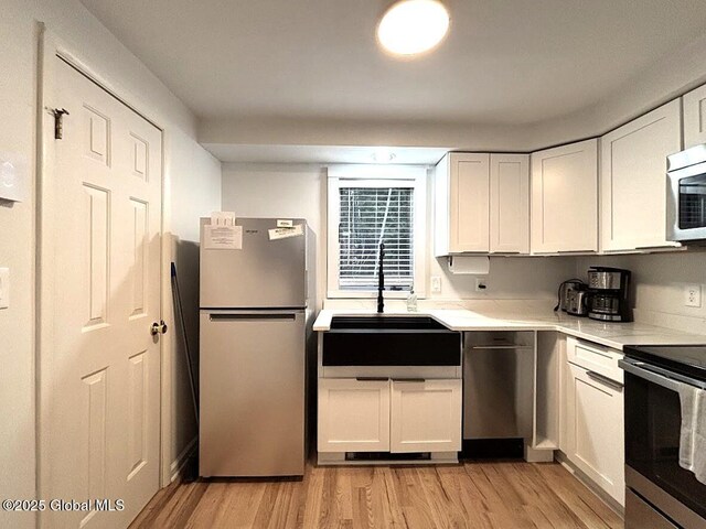 kitchen with white cabinets, light wood finished floors, a sink, and appliances with stainless steel finishes