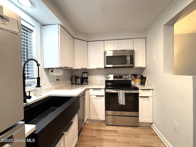 kitchen with light stone counters, a sink, light wood-style floors, stainless steel appliances, and white cabinetry