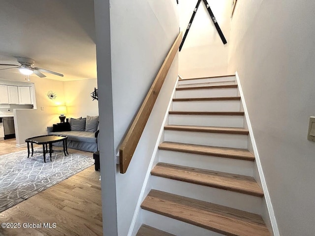 stairs featuring wood finished floors, a ceiling fan, and baseboards