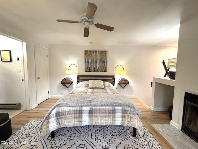 bedroom with wood finished floors, baseboards, baseboard heating, and a ceiling fan