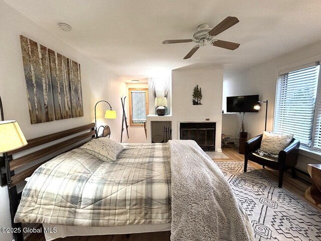 bedroom with a fireplace with flush hearth, wood finished floors, and ceiling fan