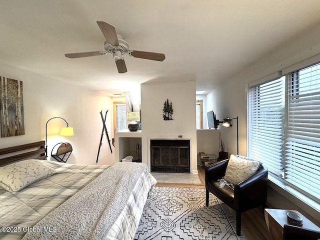 bedroom featuring wood finished floors, a glass covered fireplace, and ceiling fan