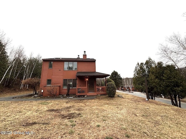 rear view of house featuring a chimney and covered porch