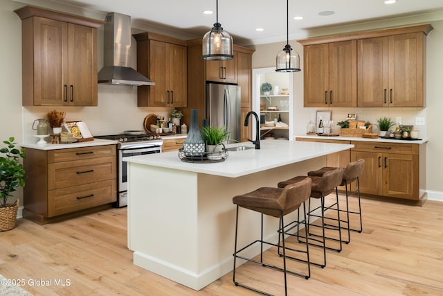 kitchen with wall chimney range hood, a sink, decorative backsplash, stainless steel appliances, and light wood finished floors
