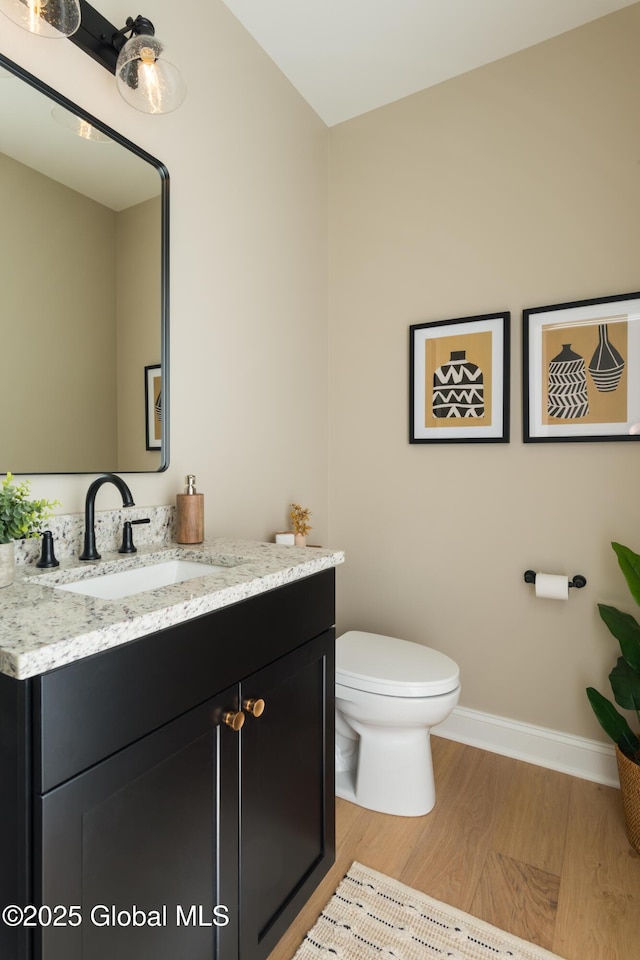 half bathroom featuring baseboards, wood finished floors, toilet, and vanity