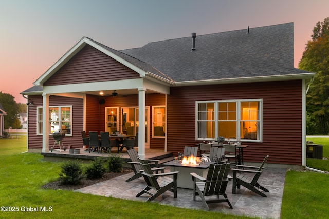 rear view of property with a fire pit, a patio, a shingled roof, and a lawn