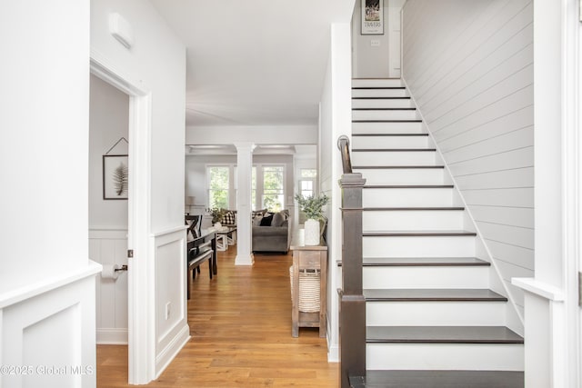 staircase featuring decorative columns, wainscoting, and wood finished floors