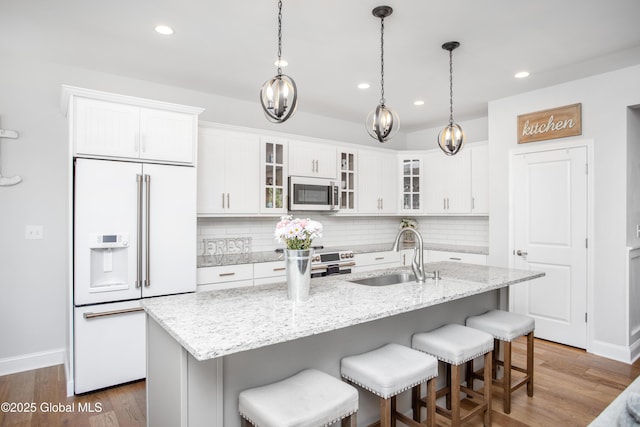kitchen featuring white cabinets, high end appliances, decorative backsplash, and a sink
