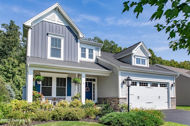 view of front of property featuring roof with shingles, an attached garage, stone siding, board and batten siding, and driveway