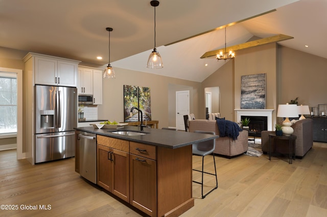 kitchen with light wood finished floors, stainless steel appliances, a sink, dark countertops, and a breakfast bar