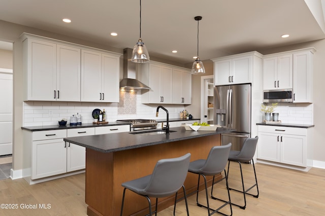 kitchen with wall chimney range hood, dark countertops, stainless steel appliances, and a sink