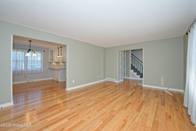 87 Dorchester Ave, Bethlehem, NY 12158 - unfurnished living room with stairway, an inviting chandelier, visible vents, and light wood-type flooring