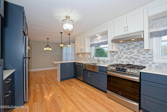 87 Dorchester Ave, Bethlehem, NY 12158 - kitchen with under cabinet range hood, a sink, a peninsula, appliances with stainless steel finishes, and white cabinetry