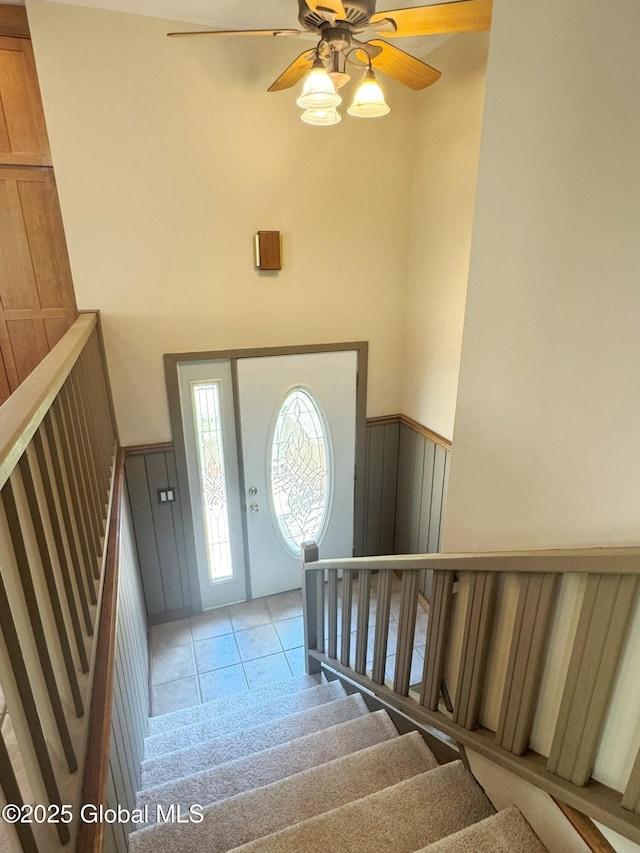 foyer featuring wainscoting, light tile patterned floors, ceiling fan, stairway, and a towering ceiling