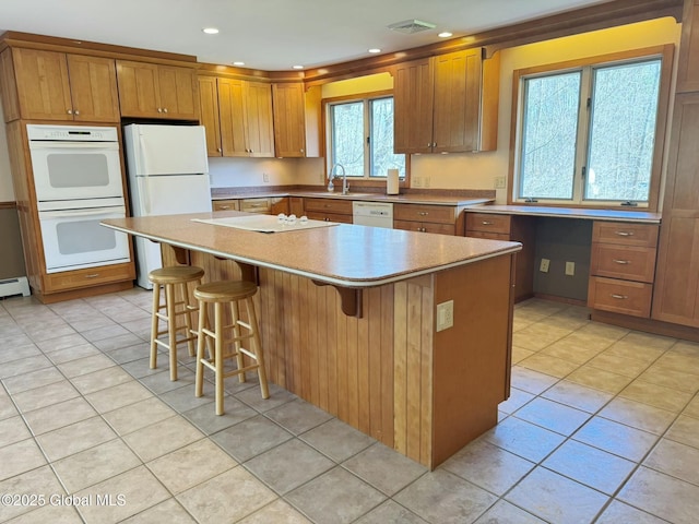 kitchen with a center island, white appliances, light tile patterned flooring, and brown cabinetry