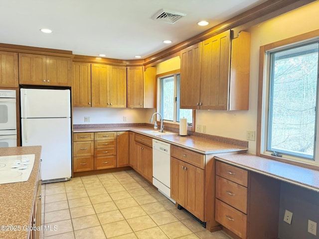 kitchen featuring a sink, brown cabinets, light tile patterned flooring, visible vents, and white appliances