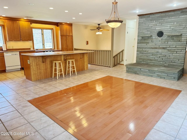 kitchen with a breakfast bar area, a kitchen island, dishwasher, a ceiling fan, and brown cabinetry