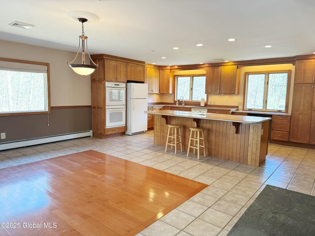 kitchen with a baseboard heating unit, light tile patterned floors, a center island, visible vents, and white appliances