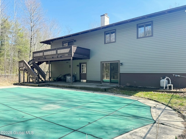 rear view of house with a wooden deck, a chimney, a patio area, a covered pool, and stairway