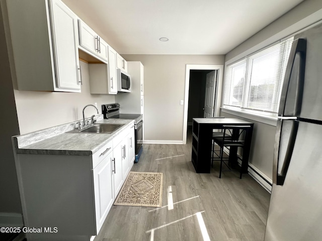 kitchen featuring white cabinets, a sink, stainless steel appliances, baseboards, and wood finished floors