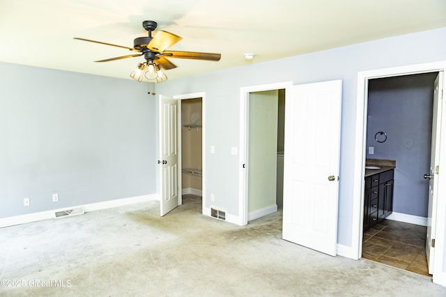 unfurnished bedroom with carpet, ensuite bath, a walk in closet, baseboards, and a ceiling fan