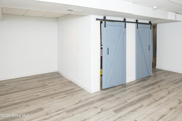 below grade area featuring a barn door, wood finished floors, baseboards, and a drop ceiling